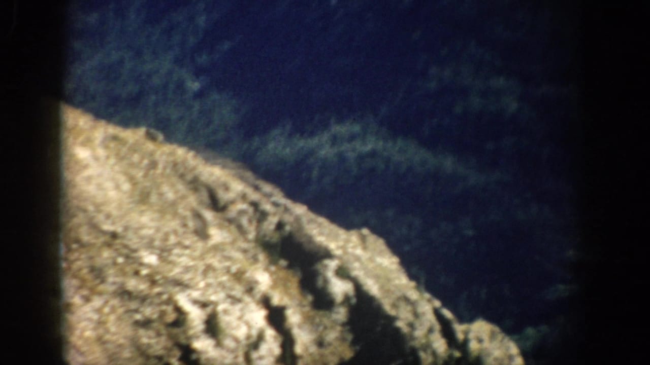 Large tan rock outcrop against dark forested mountain terrain.