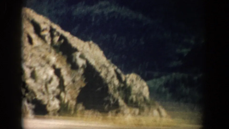 1959 Colorado 8mm frame with a rough rock formation in the foreground and dark wooded mountain terrain beyond.
