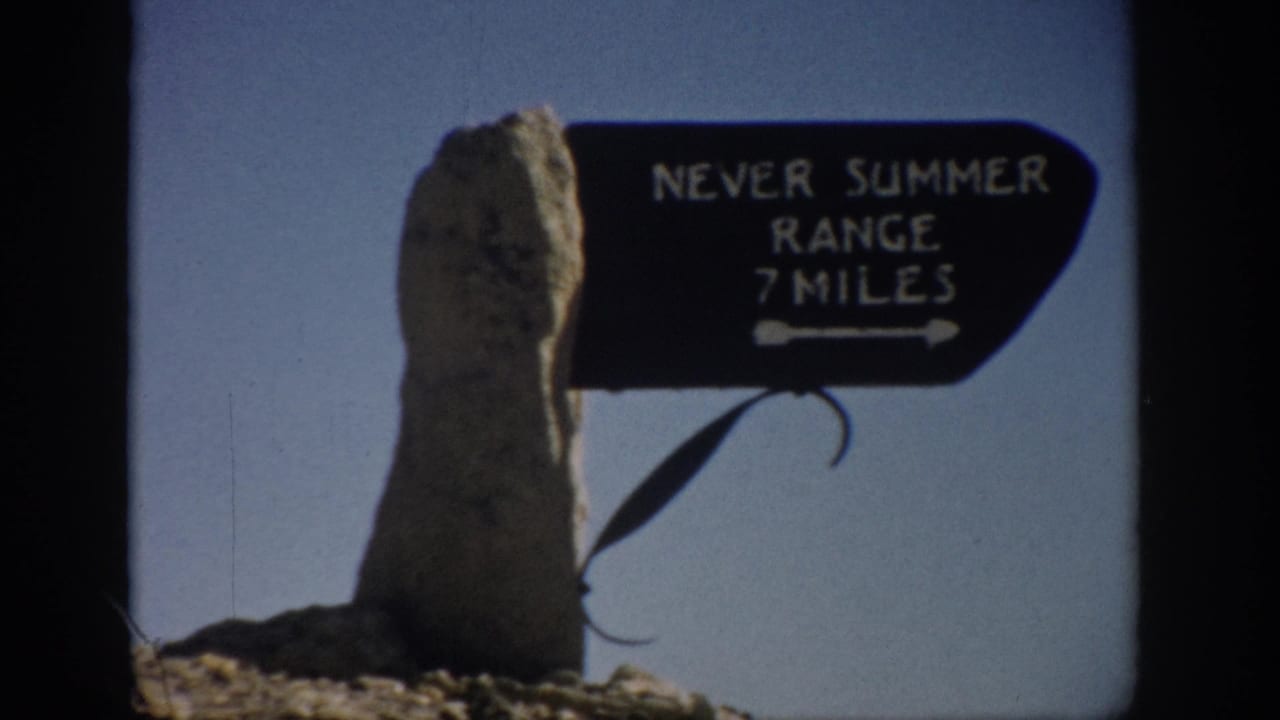 Tight 1959 Colorado home-movie view of the Never Summer Range 7 Miles sign with a rough stone post and open sky.