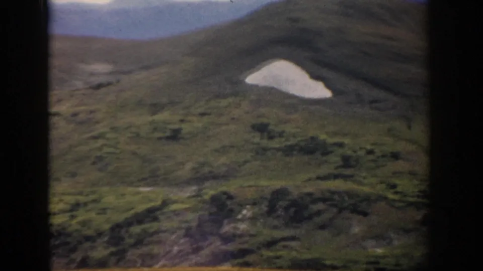 1959 Colorado mountain landscape on 8mm film, showing green slopes and a small patch of lingering snow.