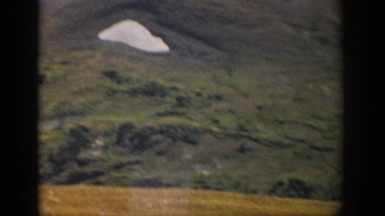 1959 Colorado 8mm view of a rounded green hillside with a pale snow or rock patch and soft home-movie focus.