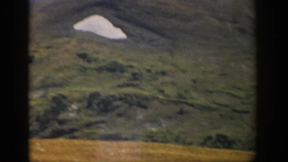 1959 Colorado 8mm view of a rounded green hillside with a pale snow or rock patch and soft home-movie focus.