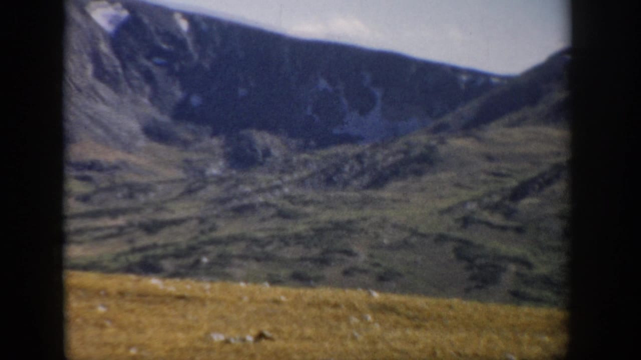 Distant mountain ridge and green-brown alpine terrain with dark vertical frame borders.