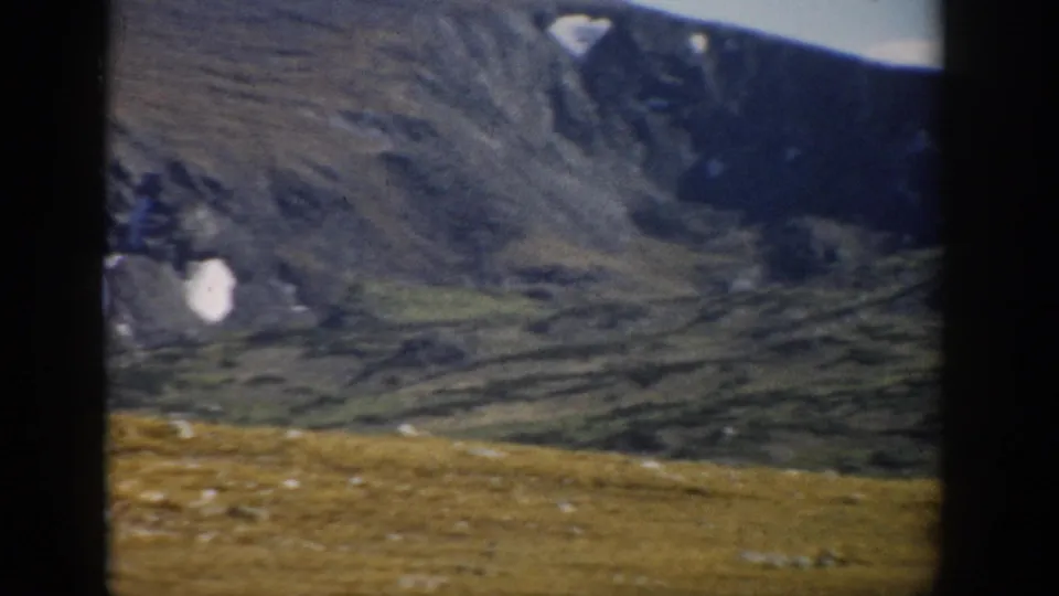 1959 Colorado 8mm frame of a high mountain basin, small snow patch, and meadow foreground during a handheld pan.