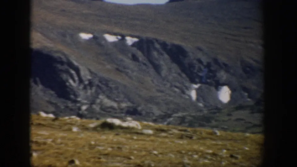 1959 Colorado Trail Ridge Road view of rocky alpine slopes with several snow patches and open high-country ground.