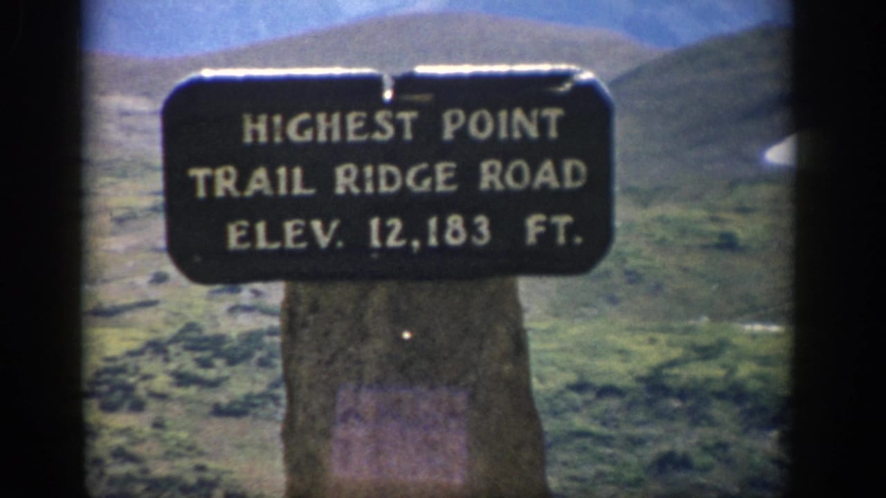 Visitor-shot 1959 Colorado frame with the 12,183-foot Trail Ridge Road sign centered before rugged high-country slopes.