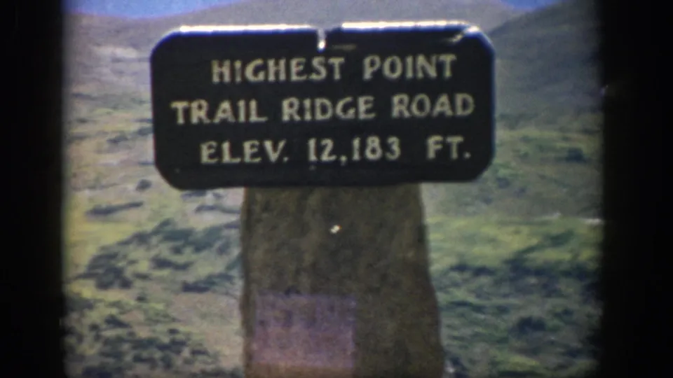 1959 Colorado 8mm shot of the highest point sign on Trail Ridge Road, with soft grain and alpine landscape in the background.