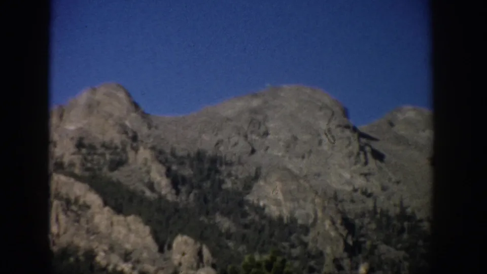 1959 Colorado 8mm view of rocky alpine terrain and sparse evergreens, with soft focus and dark border framing.