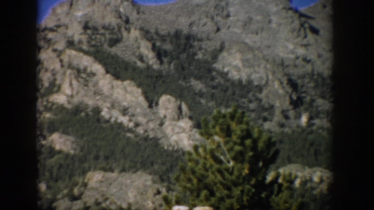 1959 Colorado 8mm frame with rugged gray rock formations, tree-covered slopes, and a dark vertical film border.