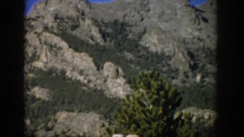 1959 Colorado 8mm frame with rugged gray rock formations, tree-covered slopes, and a dark vertical film border.