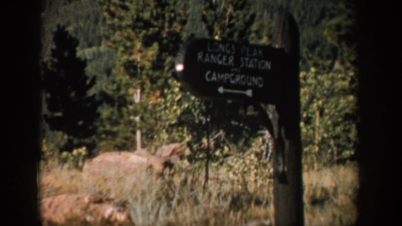 1959 Colorado 8mm frame showing a dark wooden Longs Peak Ranger Station and Campground sign in a wooded setting.