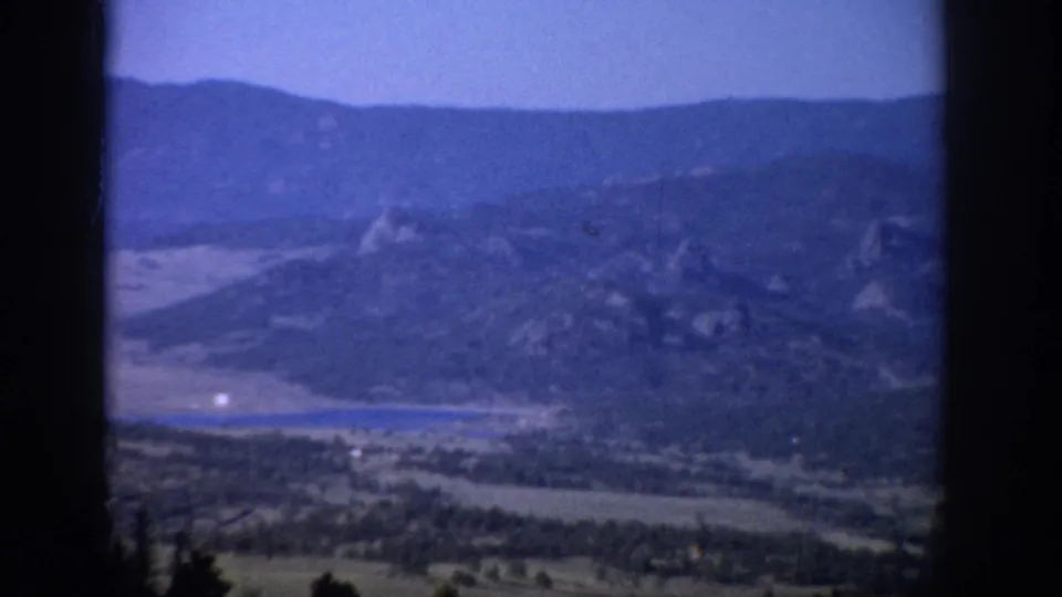 1959 Colorado 8mm frame looking through a dark window frame toward mountains, a green valley, and a small lake.