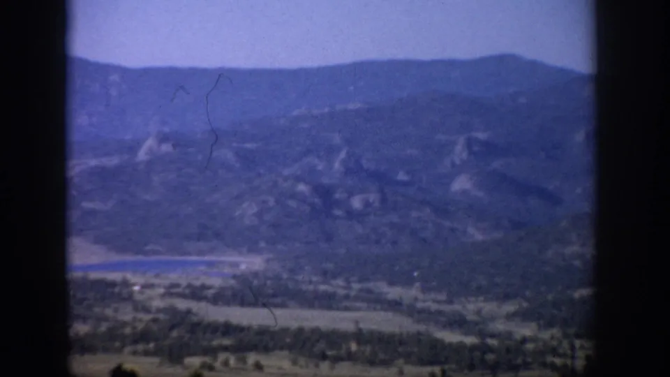 1959 Colorado 8mm view through window panes toward hazy mountains, a narrow lake, and wooded valley land.