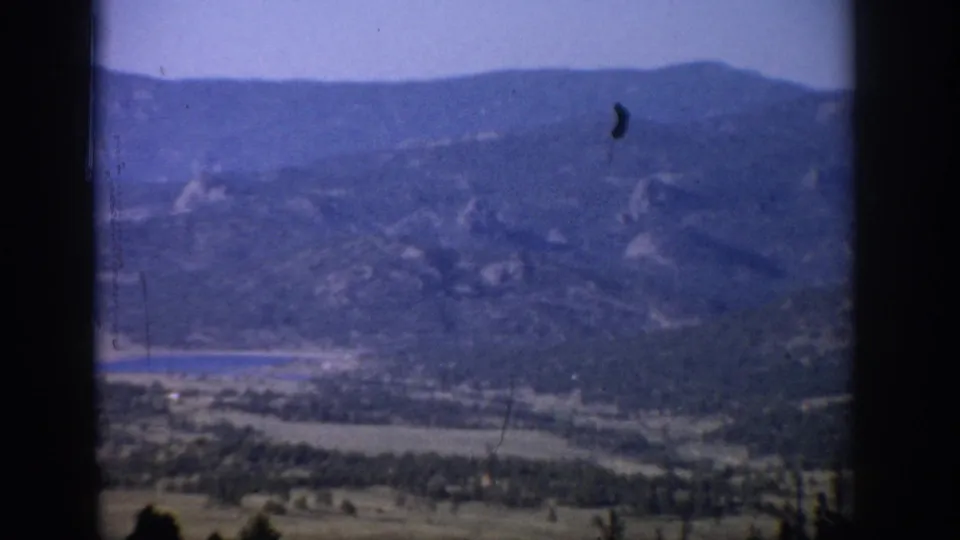 1959 Colorado home-movie still of distant mountains, a lake, and valley greenery framed by dark window edges.