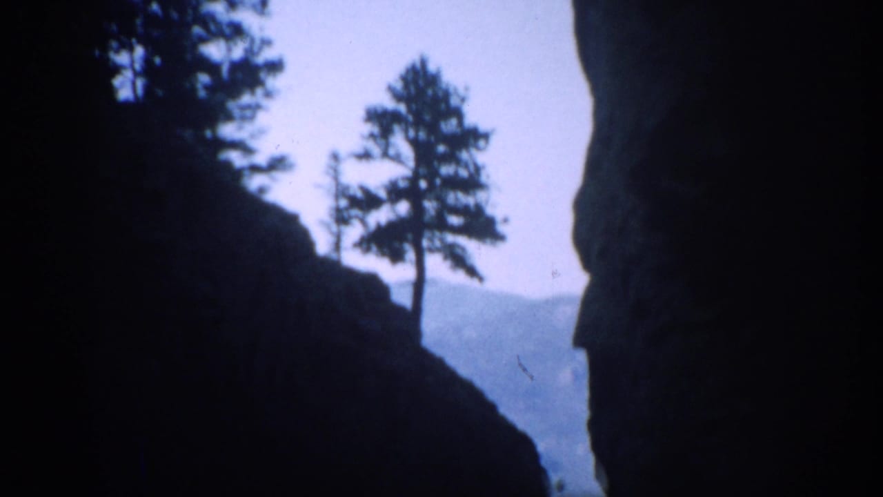 1959 Colorado 8mm frame showing dark rock walls and pine silhouettes with distant mountains beyond the canyon opening.