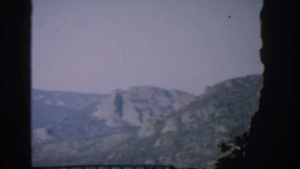 Colorado mountain valley appears between dark canyon edges in faded 8mm color footage from a moving vehicle.