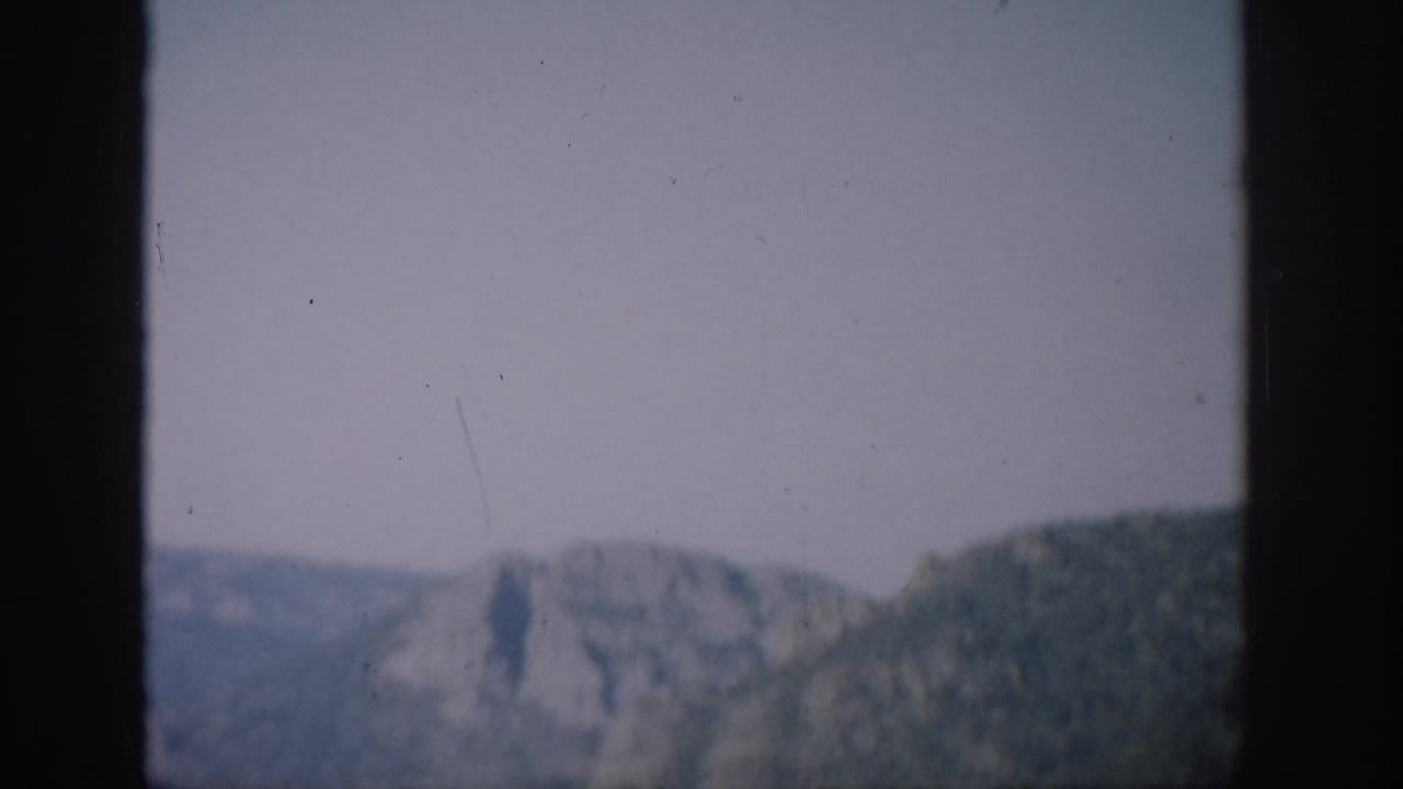 Colorado mountain terrain appears beyond a helicopter window, with a dark vertical frame cutting through the view.