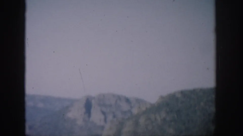 Colorado mountain terrain appears beyond a helicopter window, with a dark vertical frame cutting through the view.