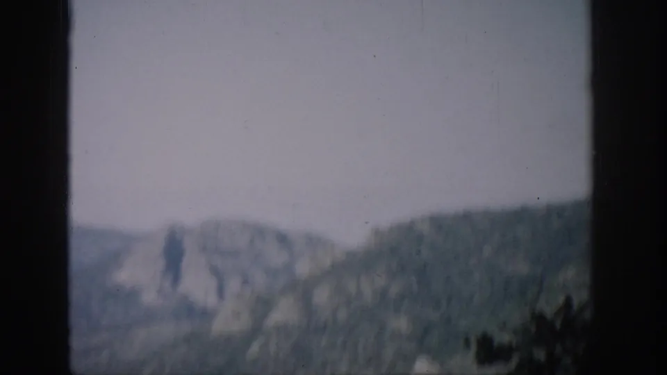 A soft 8mm Colorado aerial view shows mountain slopes through a helicopter window with visible film wear.