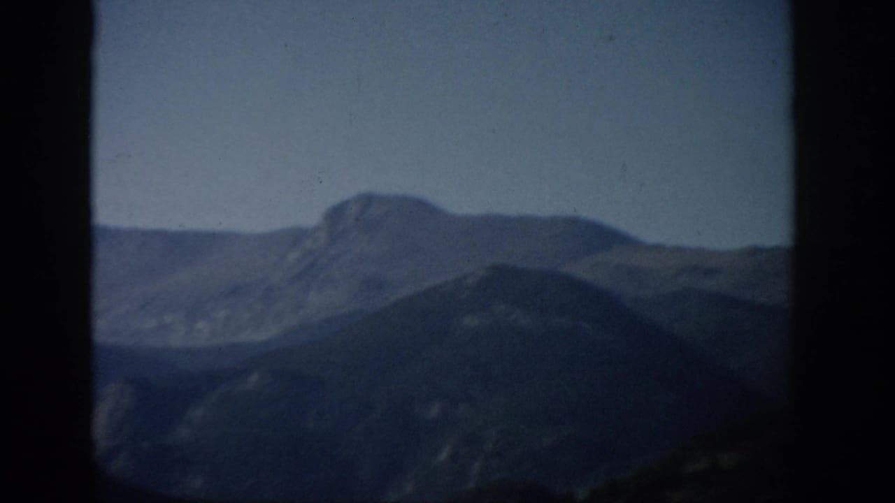 1959 Colorado 8mm frame showing layered mountain ridges and a distant peak, softly focused within dark film borders.
