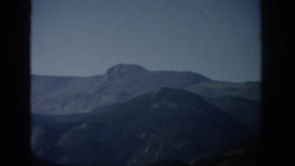 1959 Colorado 8mm frame showing layered mountain ridges and a distant peak, softly focused within dark film borders.