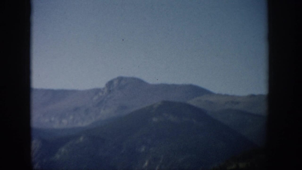 Aerial-looking 1959 Colorado mountain view with a distant rocky peak, darker ridge line, and visible 8mm border edges.
