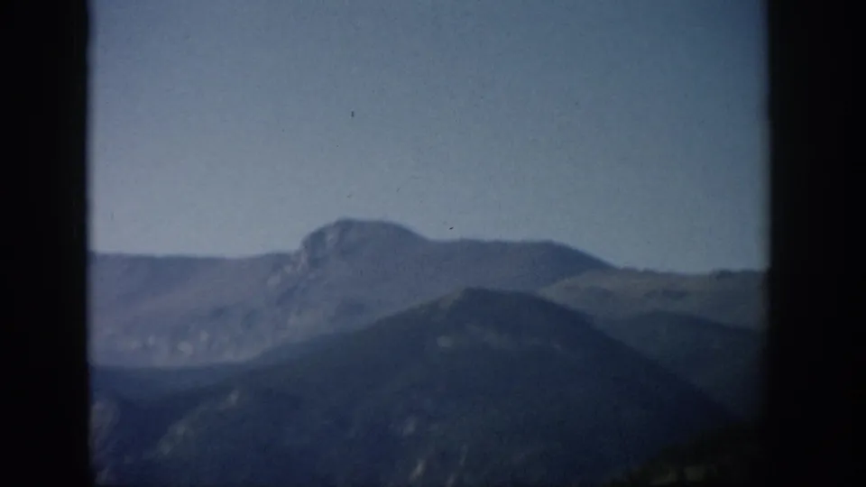 Aerial-looking 1959 Colorado mountain view with a distant rocky peak, darker ridge line, and visible 8mm border edges.