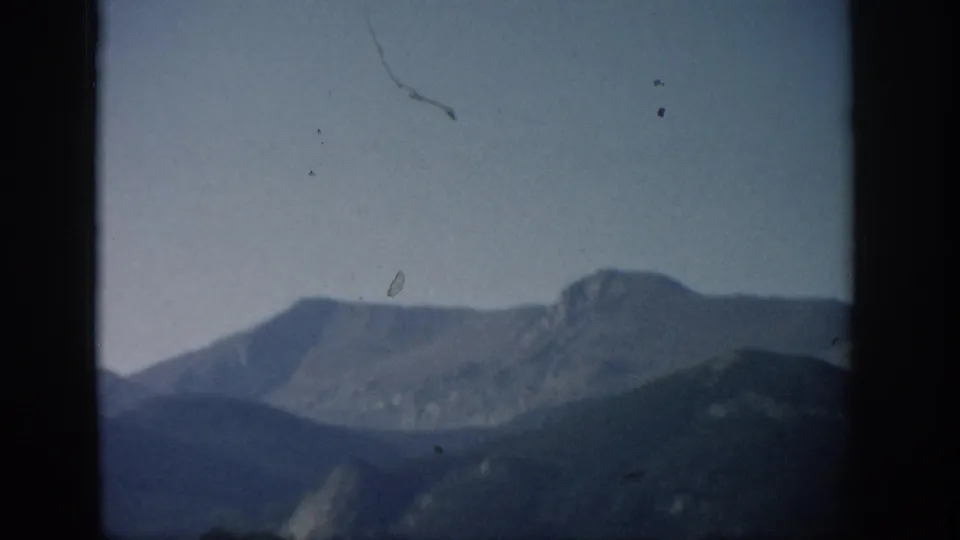 1959 Colorado 8mm still of a hazy mountain panorama with a rounded distant peak and small film scratches in the sky.
