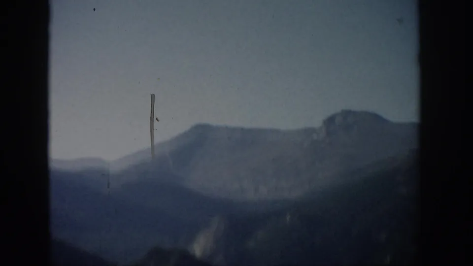 Colorado 1959 8mm frame showing a blurred mountain range, pale sky, and a prominent vertical film scratch near center.