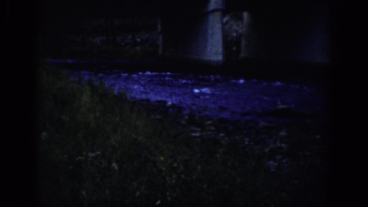 1959 Colorado 8mm frame showing a shadowed riverbank, rippling water, and part of a concrete bridge under blue-purple night lighting.