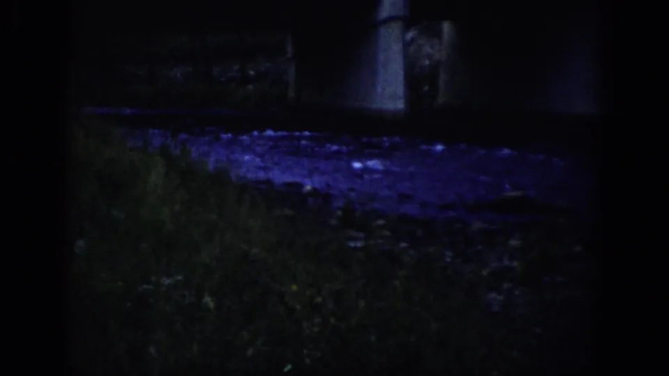 1959 Colorado 8mm frame showing a shadowed riverbank, rippling water, and part of a concrete bridge under blue-purple night lighting.