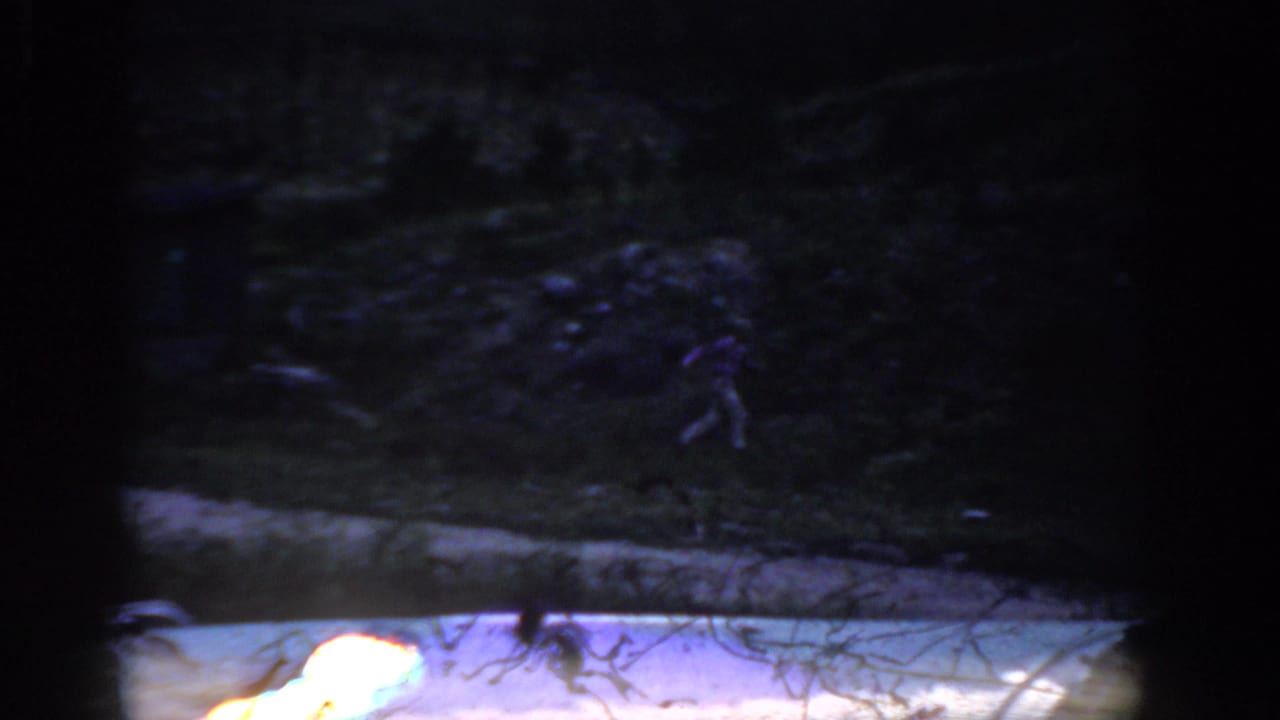 1959 Colorado home-movie frame showing a dark shoreline or bank beside lake water, with soft exposure and visible 8mm frame edges.