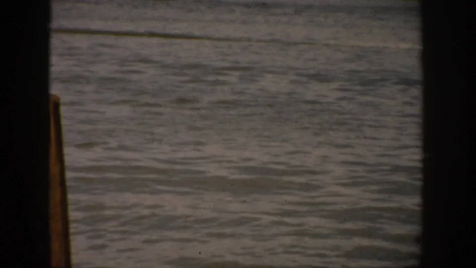 The 1959 Colorado lake scene shows open rippled water and a foreground wooden post, seen through soft faded 8mm film.
