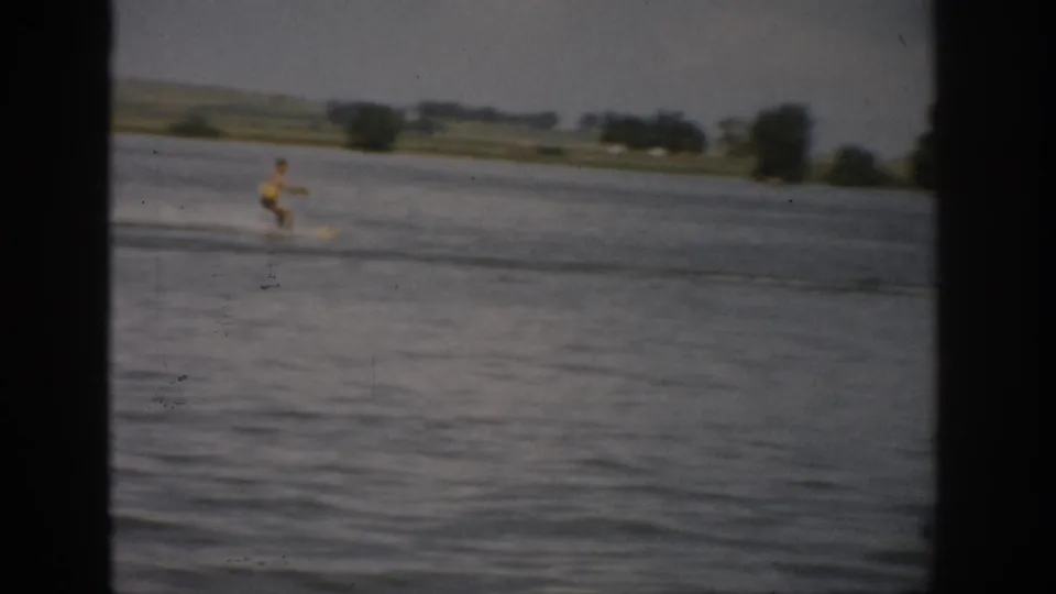 1959 Colorado home-movie frame with a water skier in a yellow swimsuit gliding across the lake and trailing wake.