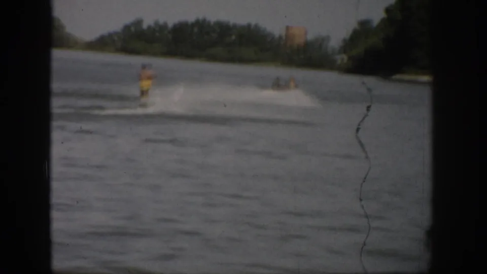 A water skier appears mid-lake in the 1959 Colorado footage, leaving spray behind as the distant shore stays soft in focus.