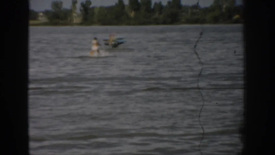 The final 1959 Colorado frame shows distant boaters and figures on the lake, framed by 8mm gate edges and a tree-lined shore.