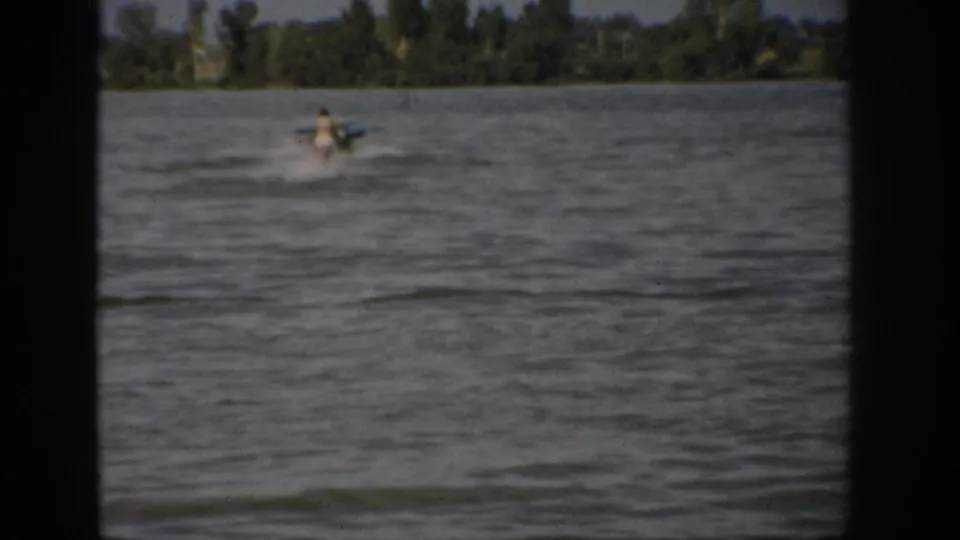A woman appears to water ski behind a motorboat on a windy Colorado lake in 1959 color 8mm footage.