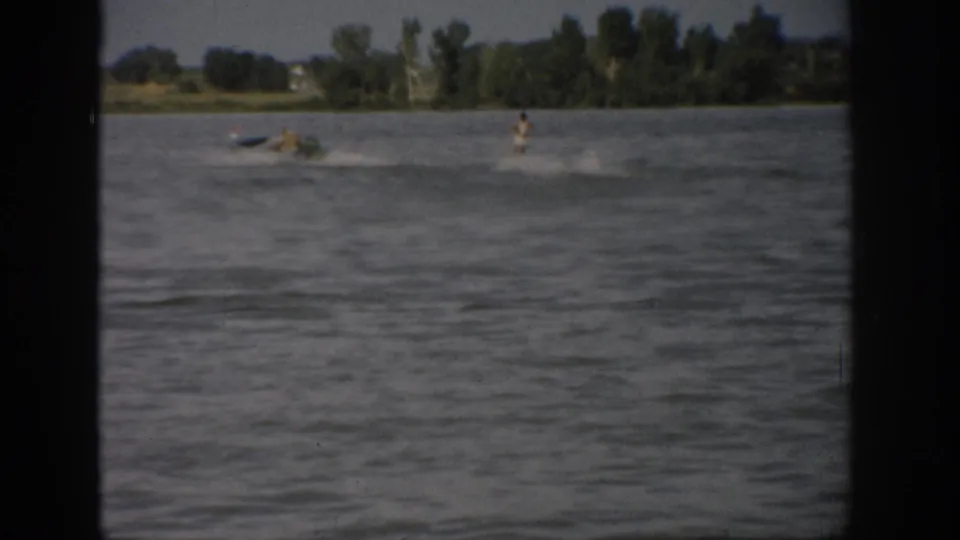 A distant woman water skiing behind a motorboat on a Colorado lake, framed by 8mm home-movie borders.