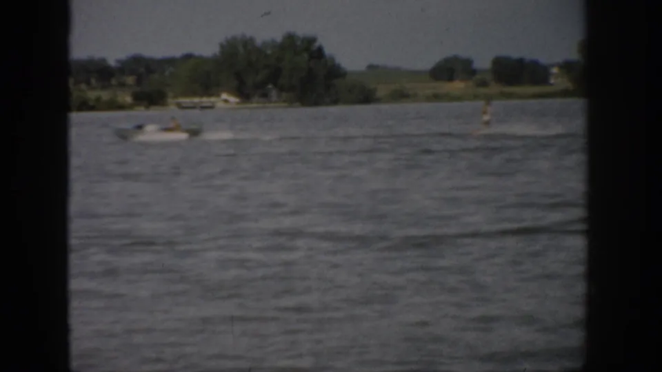 1959 Colorado lake scene showing a small motorboat on open water with trees, fields, and dark frame edges in the distance.