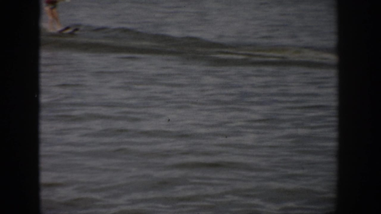 1959 Colorado 8mm frame showing a distant person on lake water, partly cropped by dark gate edges.