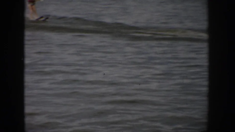 1959 Colorado 8mm frame showing a distant person on lake water, partly cropped by dark gate edges.