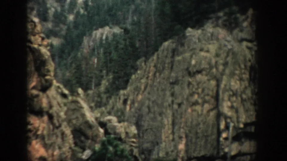 1959 Colorado 8mm view of a high rock wall and forested canyon slope, partially obscured by dark foreground edges.