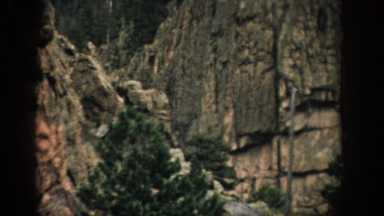 Rocky mountain cliff with evergreen trees and dark frame borders.