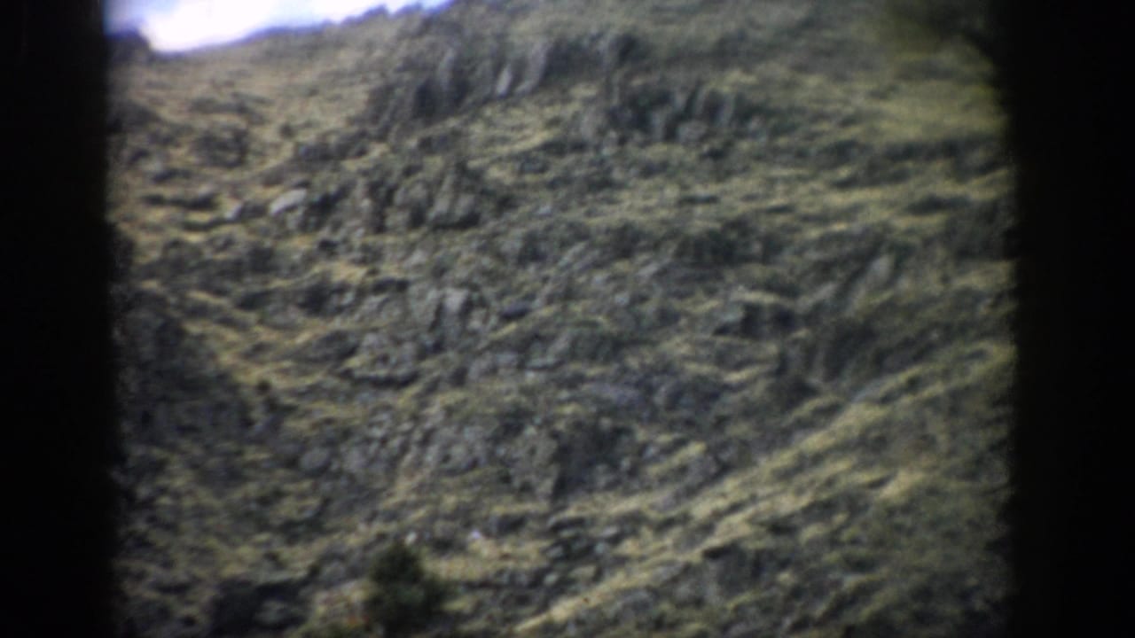 1959 Colorado home-movie frame showing a rocky mountain slope with sparse vegetation and soft, grainy color.