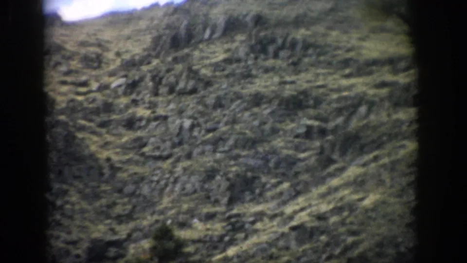 1959 Colorado home-movie frame showing a rocky mountain slope with sparse vegetation and soft, grainy color.