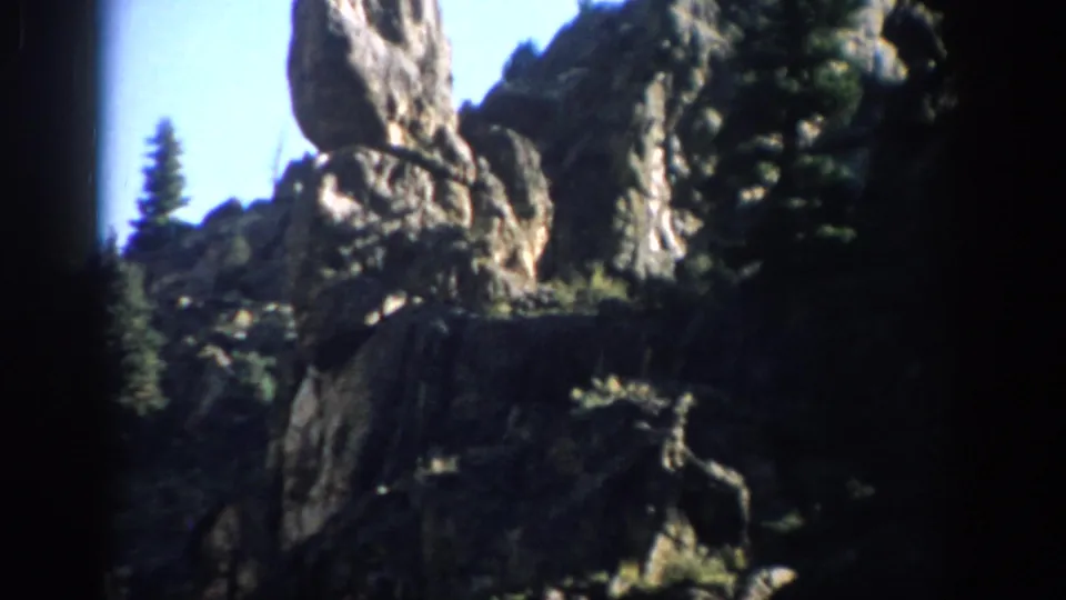1959 Colorado 8mm view of rugged rock formations with pines and blue sky, framed by dark film edges.