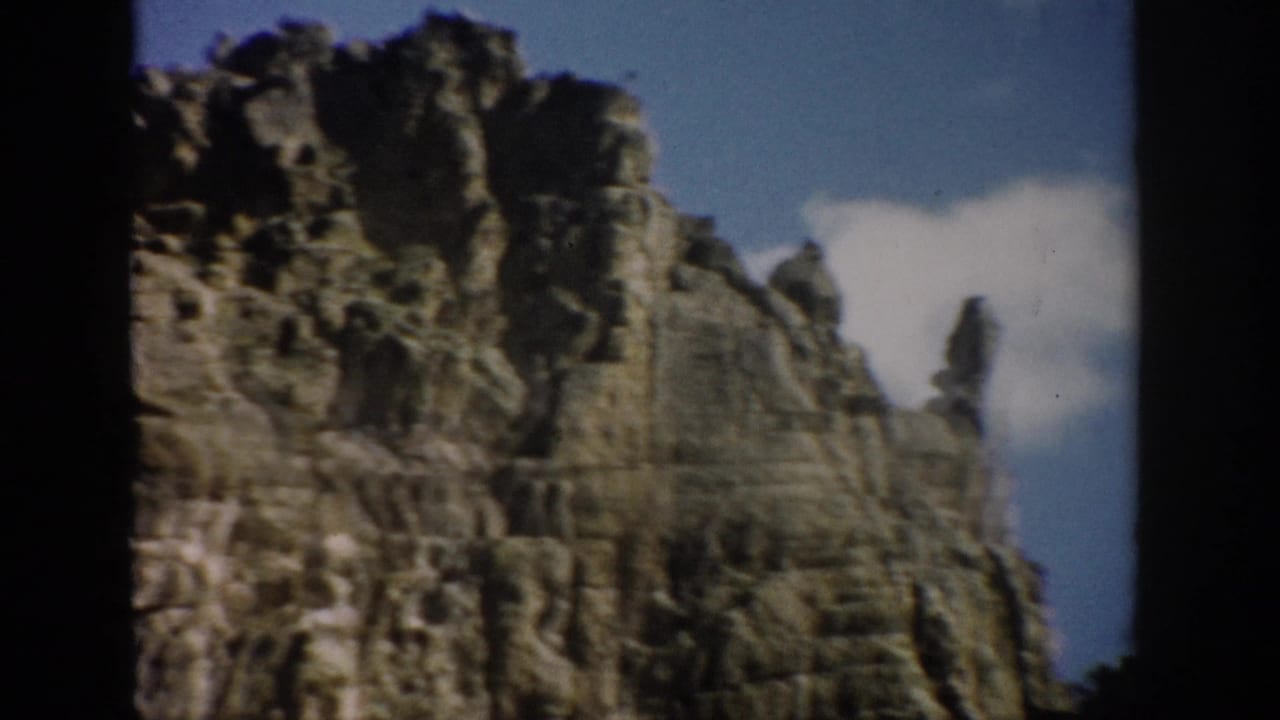 Layered rock wall and cliff top under blue sky with a bright cloud.