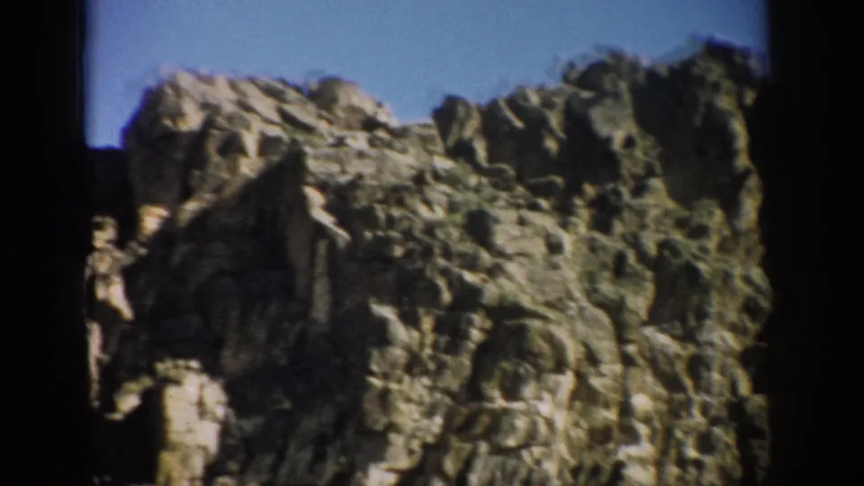 1959 Colorado 8mm frame showing a close, soft-focused view of weathered stone, shadowed hollows, and sparse vegetation.