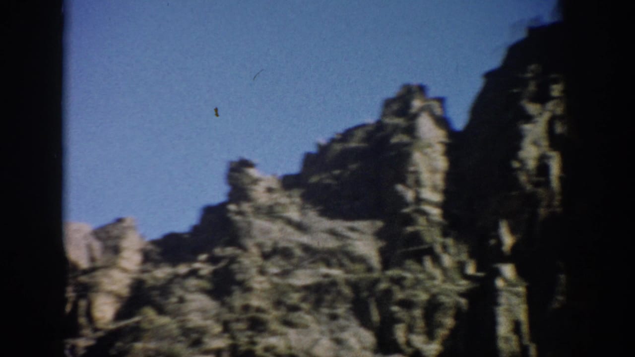 Jagged rocky hills under a bright blue sky, with dark film borders at the edges.