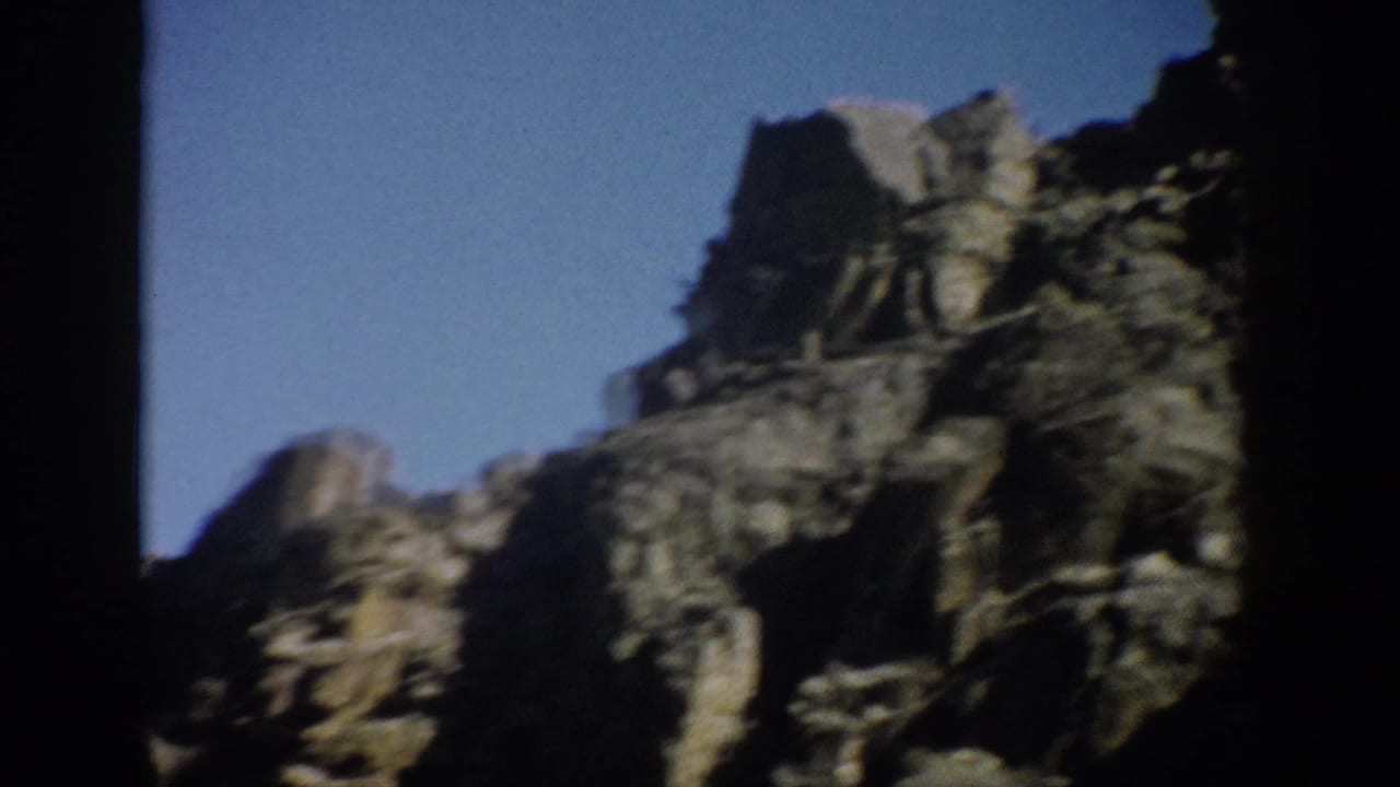 Handheld 1959 Colorado landscape frame with steep rock faces, sparse vegetation, and strong dark borders from the film scan.